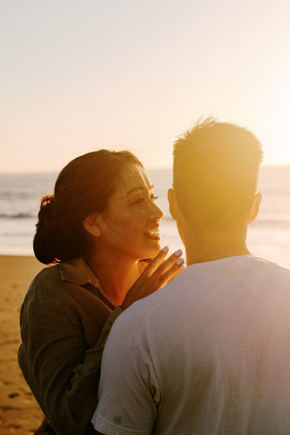 Couple sharing a laugh together on the beach during golden hour.