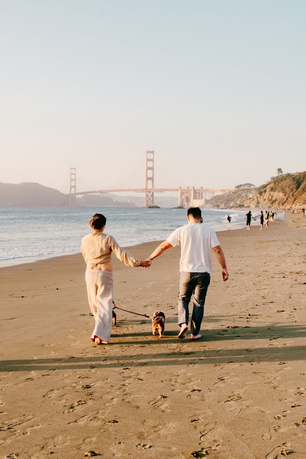 Couple walking their dog on Baker Beach with the Golden Gate Bridge in the background.