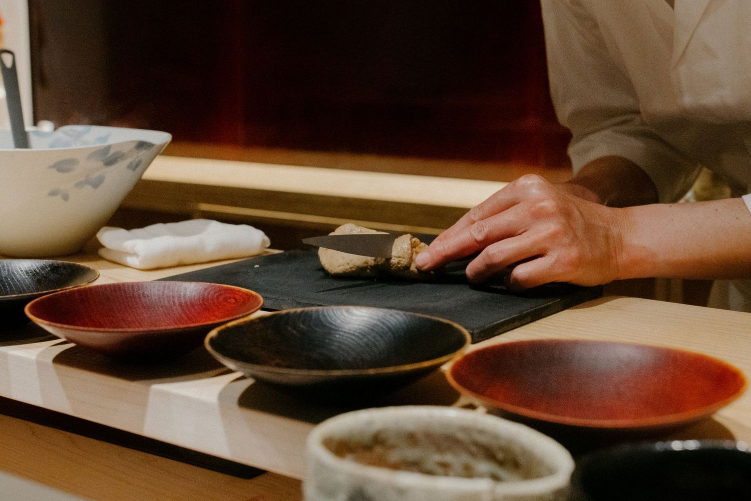 Professional sushi preparation area with red and black plates arranged on wooden counter.
