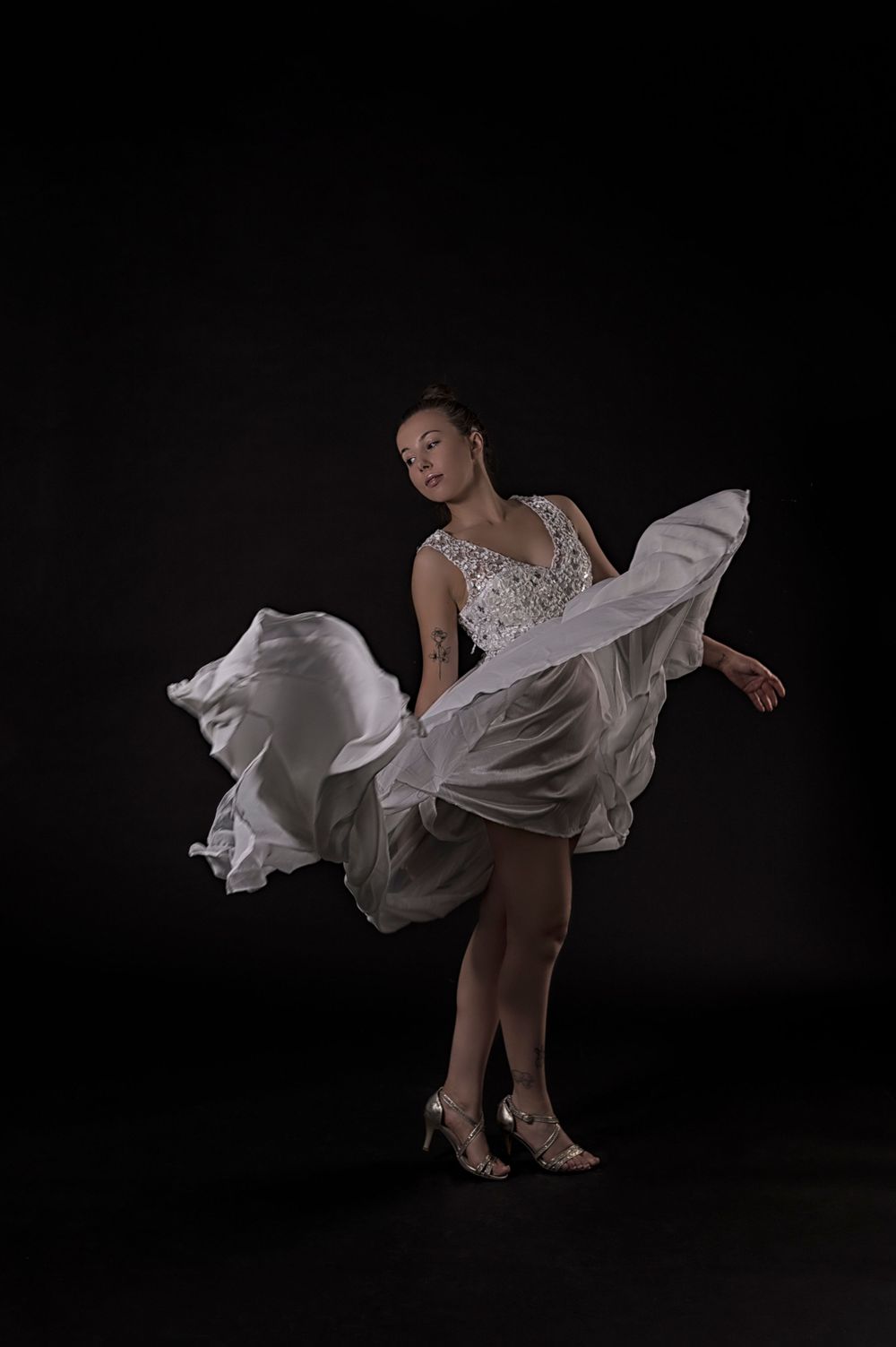 A dancer in a flowing white dress performs an elegant pose against a dark background.