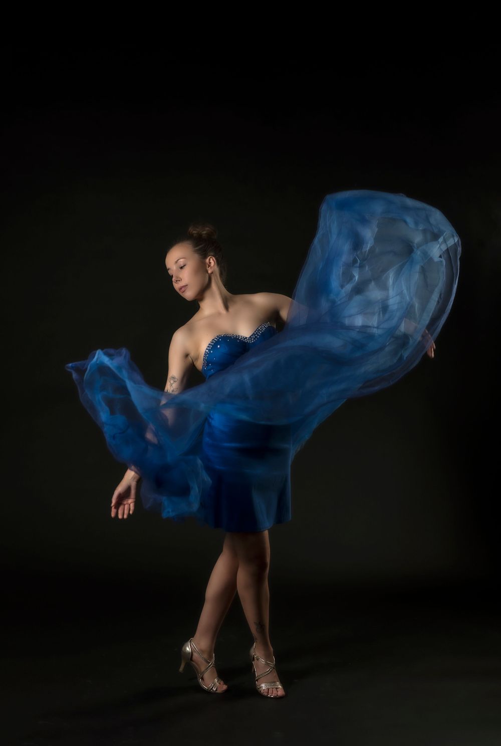 Ballet dancer in blue tulle dress poses dramatically against black backdrop.