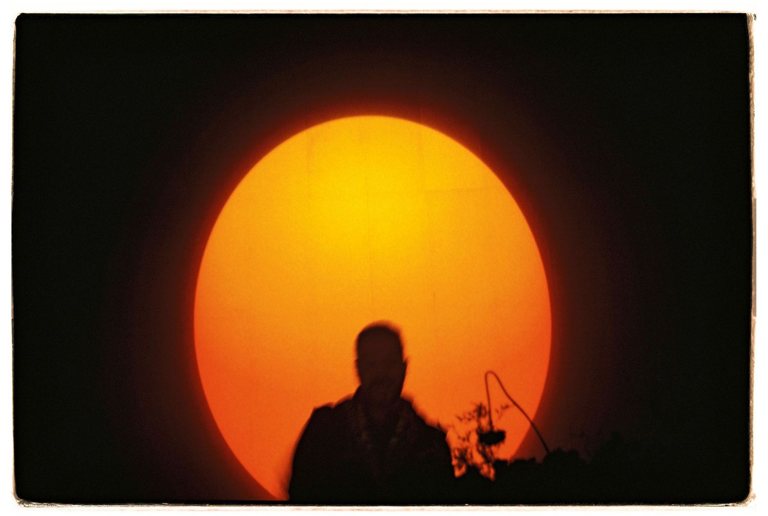 Silhouette against large orange sunset shows figure with camera equipment.