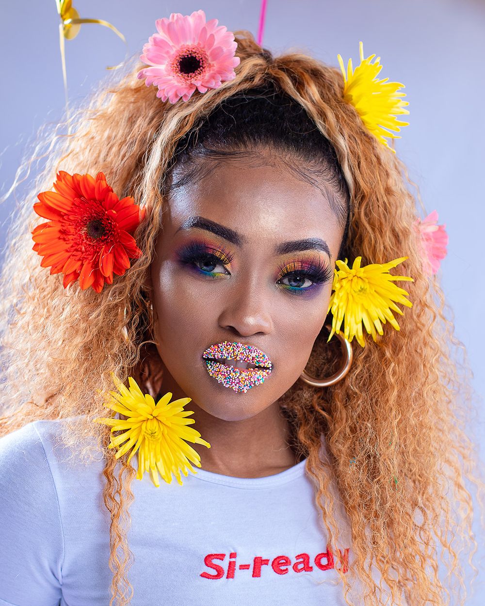 Creative beauty portrait with colorful gerbera daisies and glitter makeup against blue background.