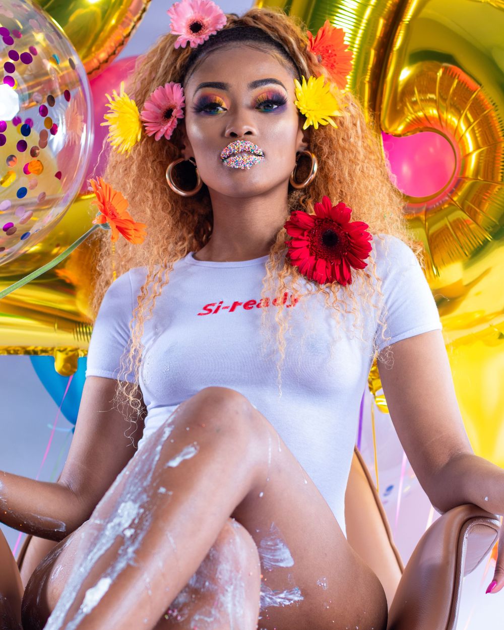 Artistic portrait with floral accessories and glitter makeup against balloon backdrop.