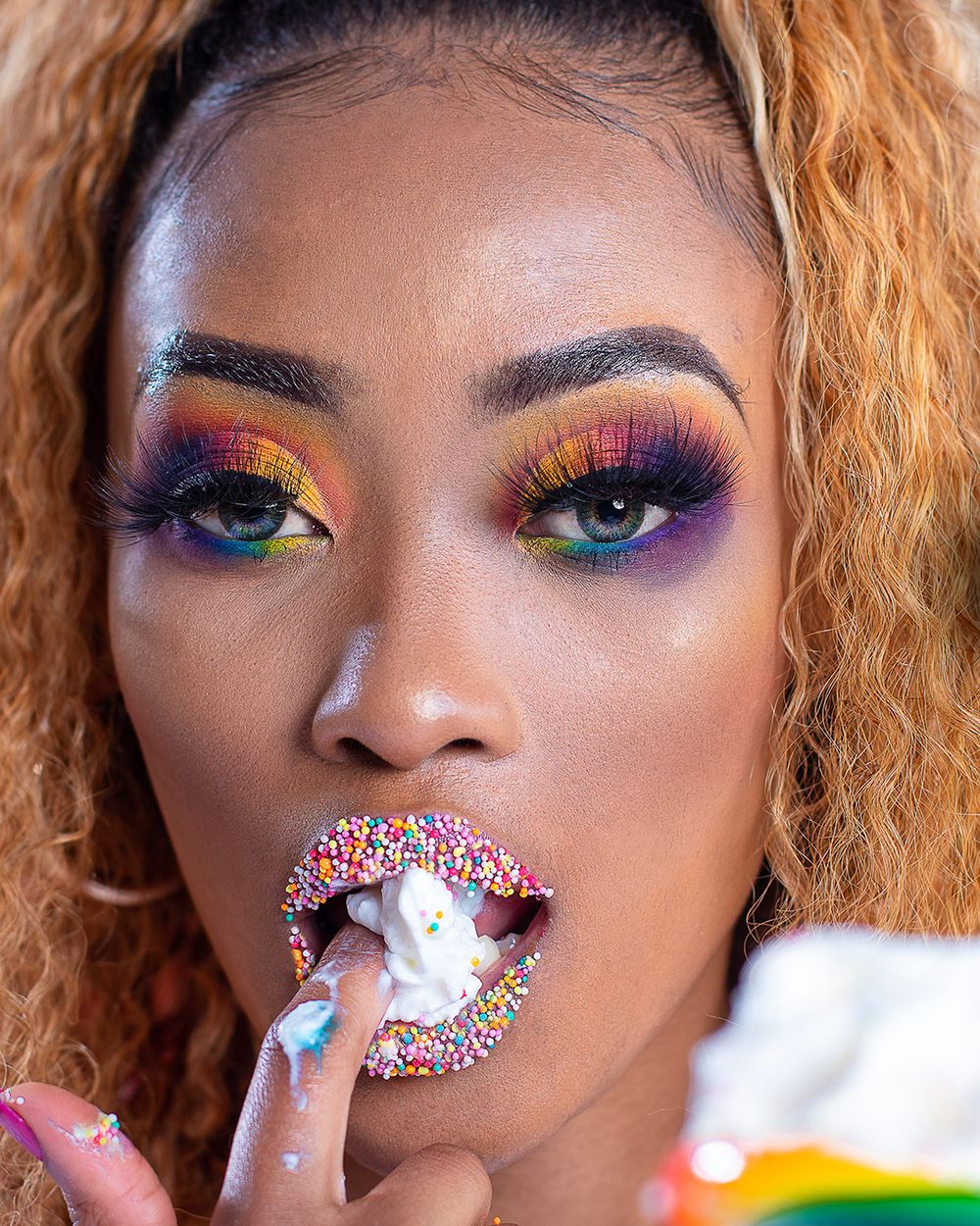 Close up beauty shot showcasing colorful rainbow eyeshadow and crystal-adorned lip makeup.