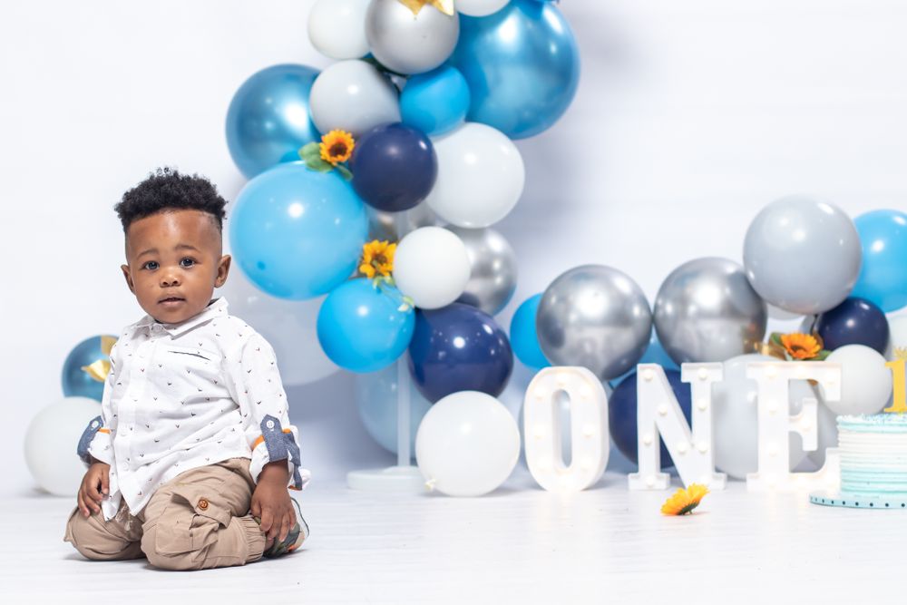 Baby sitting near blue and white balloon arch with 'ONE' text display.