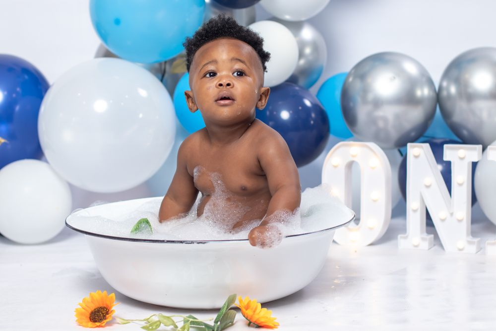 Baby in bath photoshoot with blue balloon decor and ONE letters.
