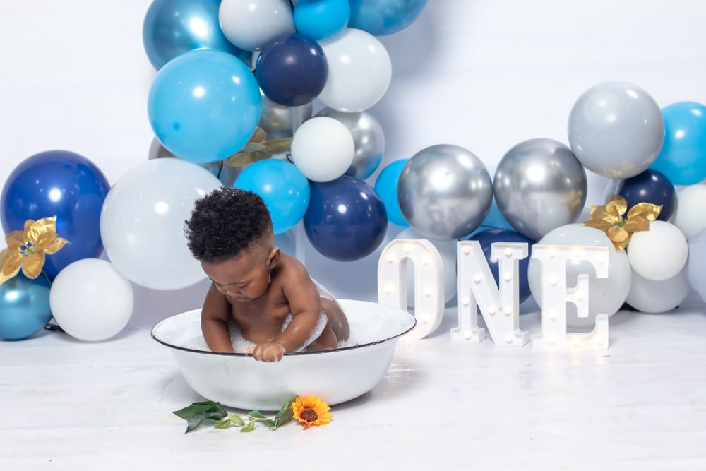 Baby lying in white basin with sunflower and balloon decorations.