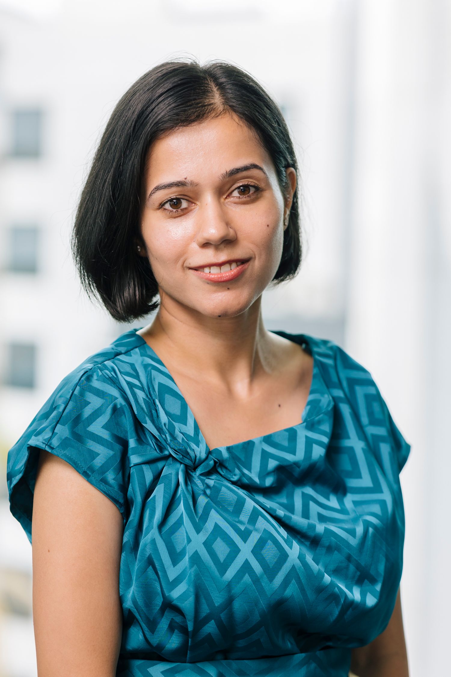 Professional in teal patterned blouse against bright office background.