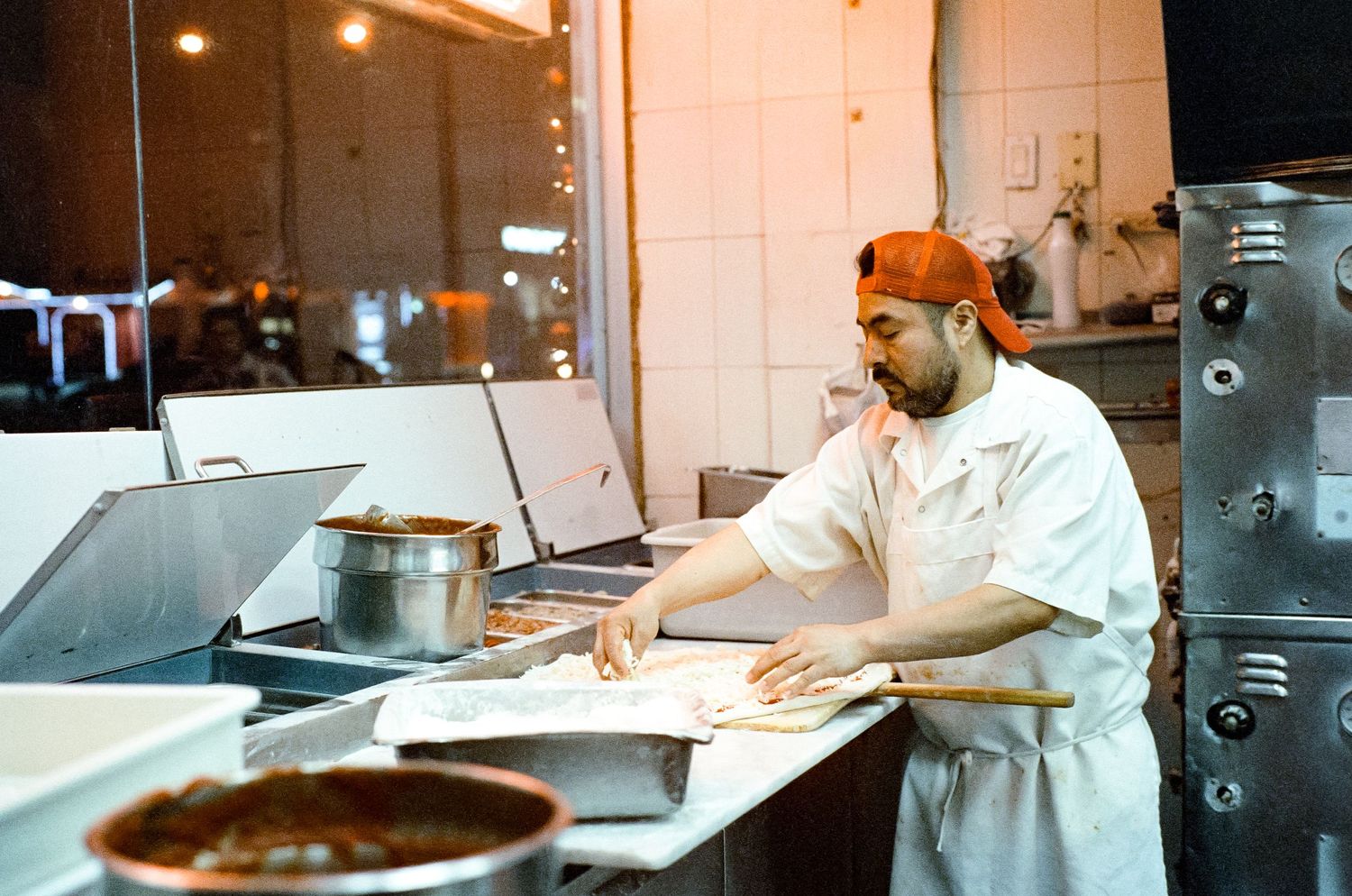 Kitchen worker preparing food at a commercial prep station with pots and equipment.