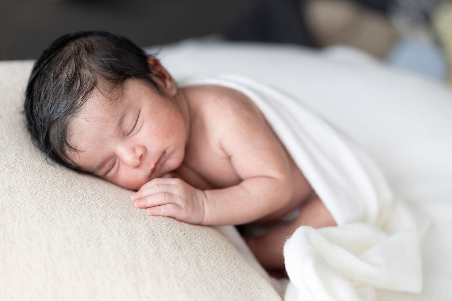 A peaceful sleeping newborn baby lies nestled in soft white bedding.