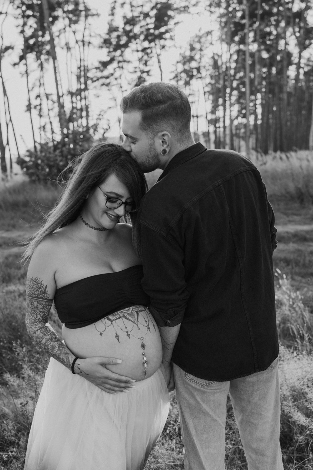 Black and white maternity photo of couple embracing in a wooded setting.