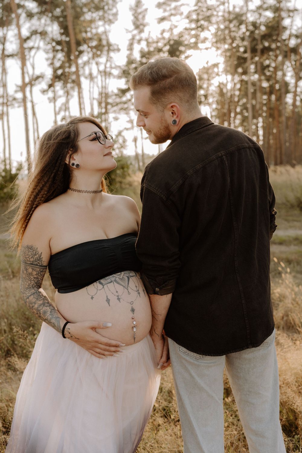 Couple shares tender moment during outdoor maternity photoshoot in a forest setting.