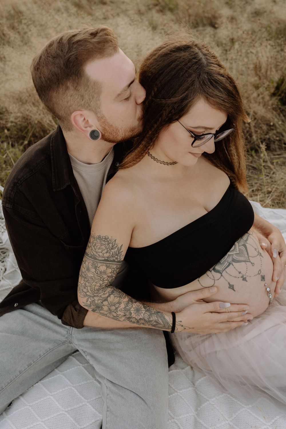 A romantic couple shares an intimate moment in a field during a maternity photoshoot.