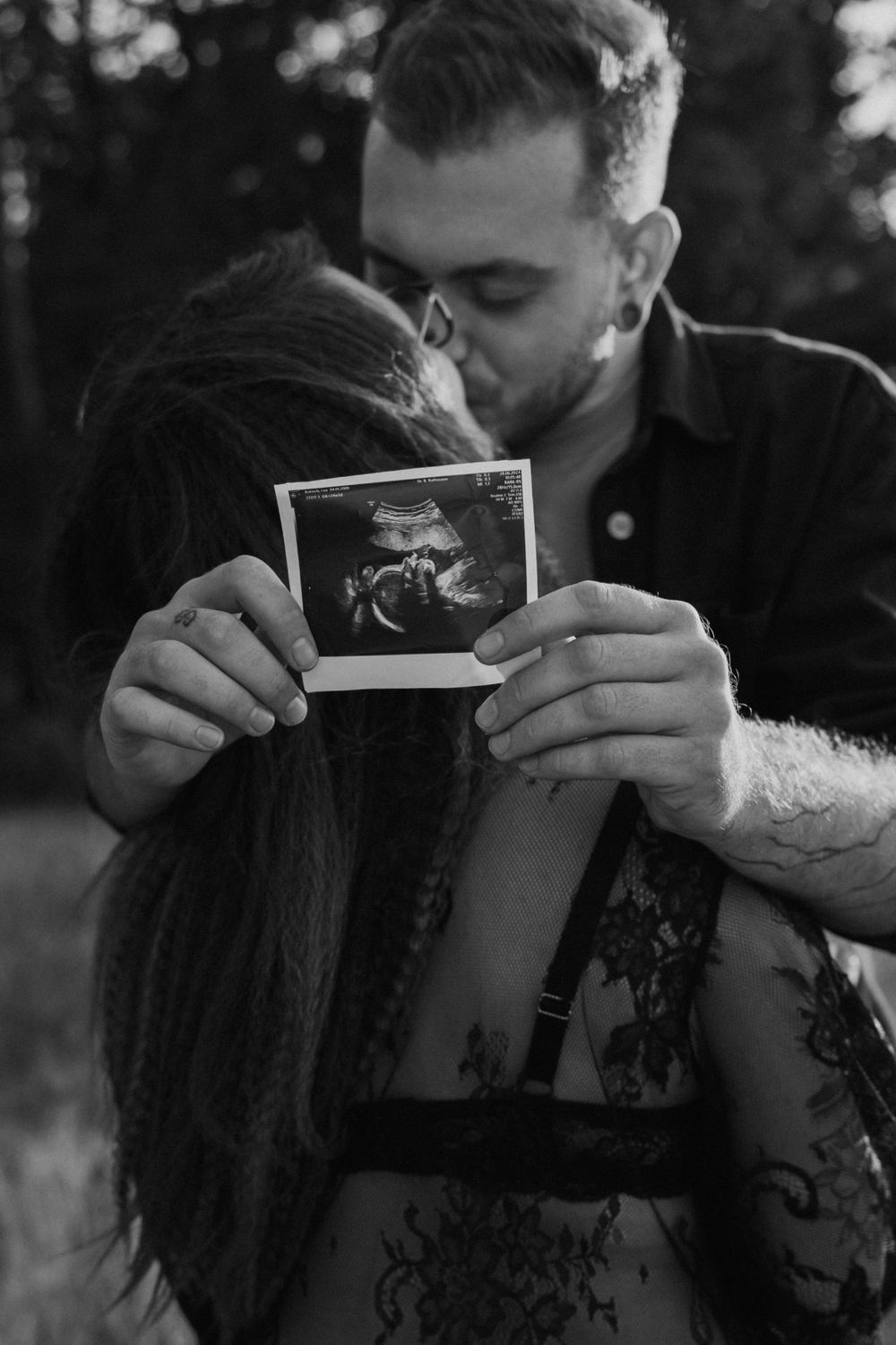 Couple holding ultrasound photo during outdoor pregnancy announcement shoot.