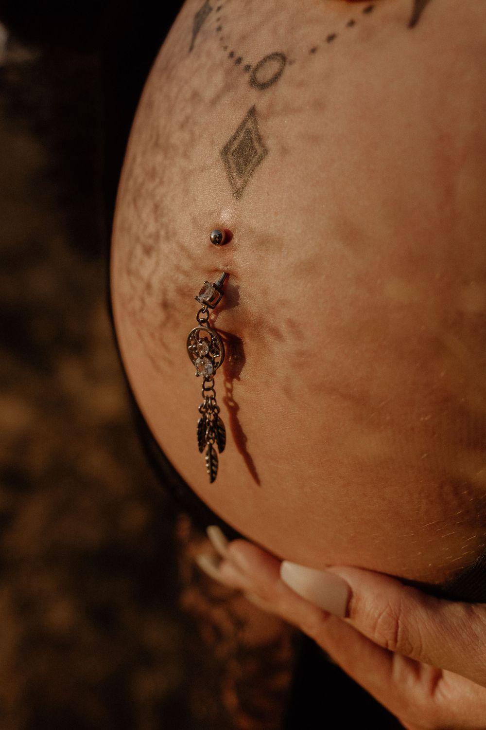Close-up of pregnant belly with decorative belly button jewelry and tattoos.