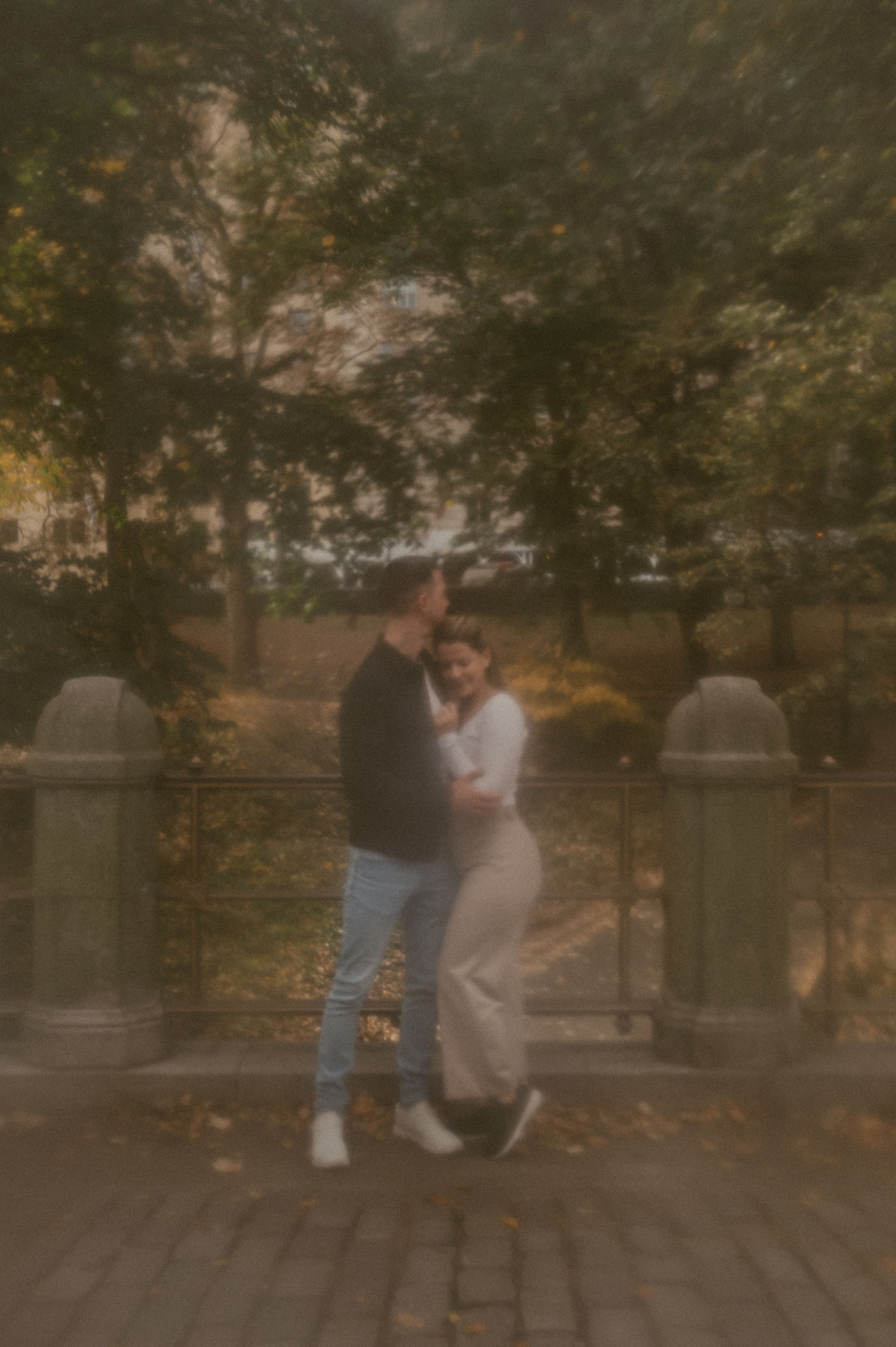 A romantic couple embraces on a brick pathway under autumn trees in a dreamy vintage-style photo.