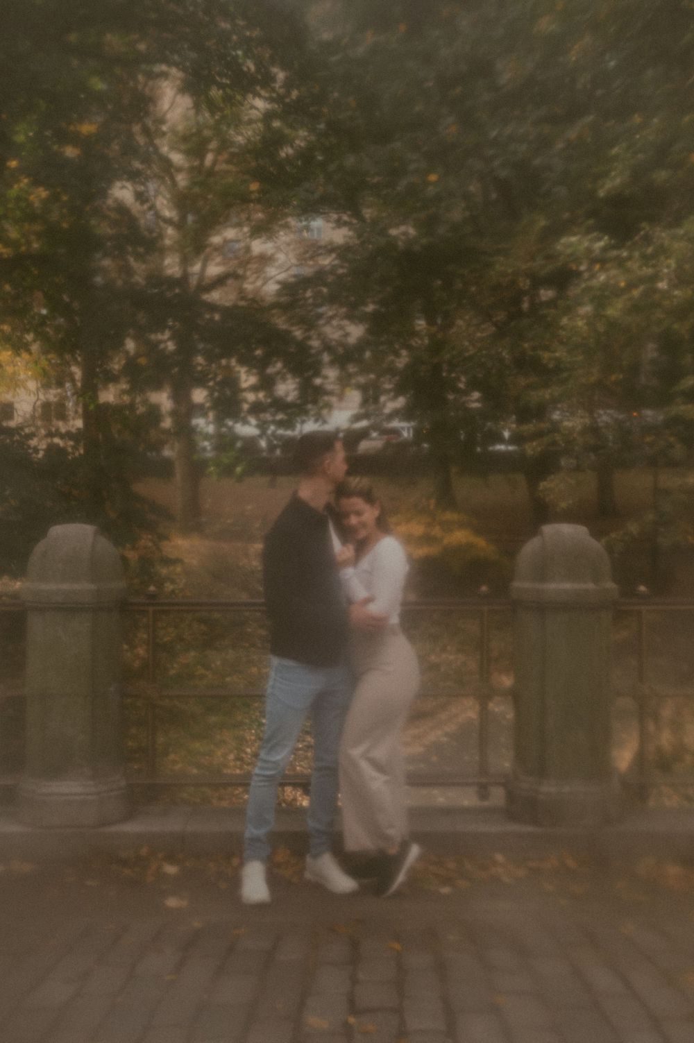 A romantic couple embraces on a brick pathway under autumn trees in a dreamy vintage-style photo.