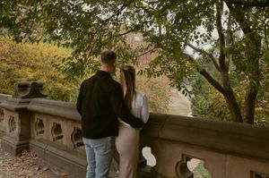 A couple sharing a romantic moment while overlooking a park from a stone bridge during autumn.