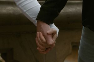 Two people holding hands together in an intimate moment against a dark background.