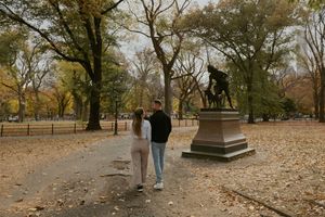 People walking through a scenic fall landscape with trees shedding their autumn leaves.