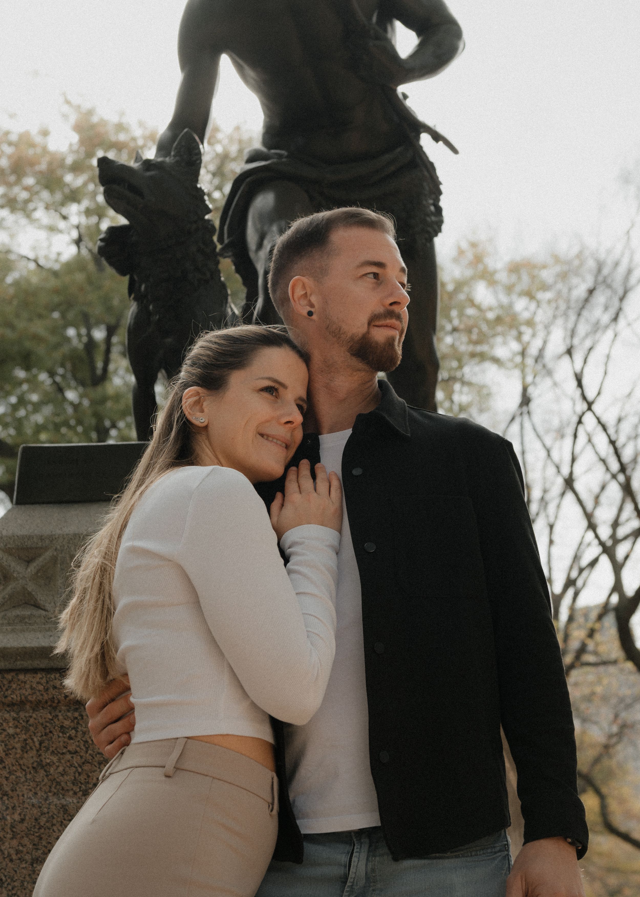 A romantic couple embraces near a statue in a park on an autumn day.