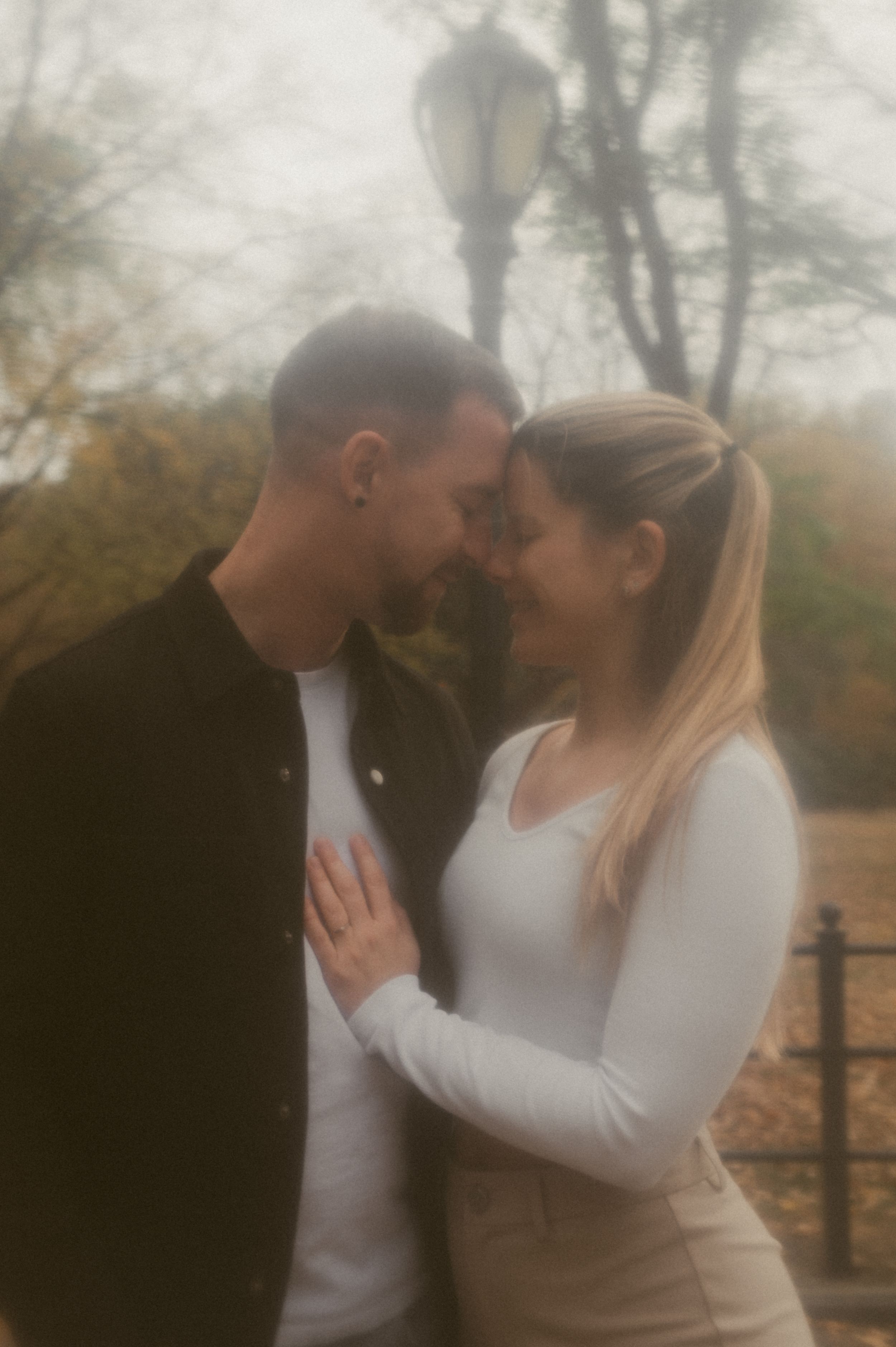 An intimate moment between a couple beneath a vintage lamppost in a misty park setting.