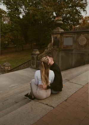 A couple reclines on stone steps surrounded by autumn foliage and architecture.