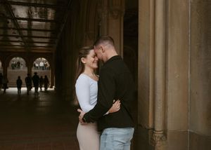 A romantic couple embraces in a dimly lit stone archway corridor with gothic architectural details.