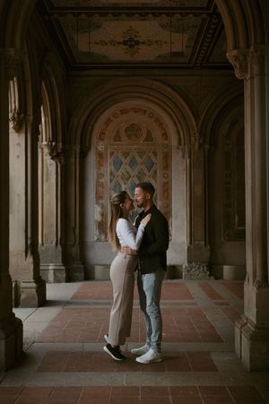 Couple embracing in an ornate architectural passageway with arched ceilings and decorative columns.