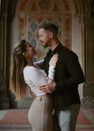 A couple shares an intimate embrace in front of decorative architectural details and arches.