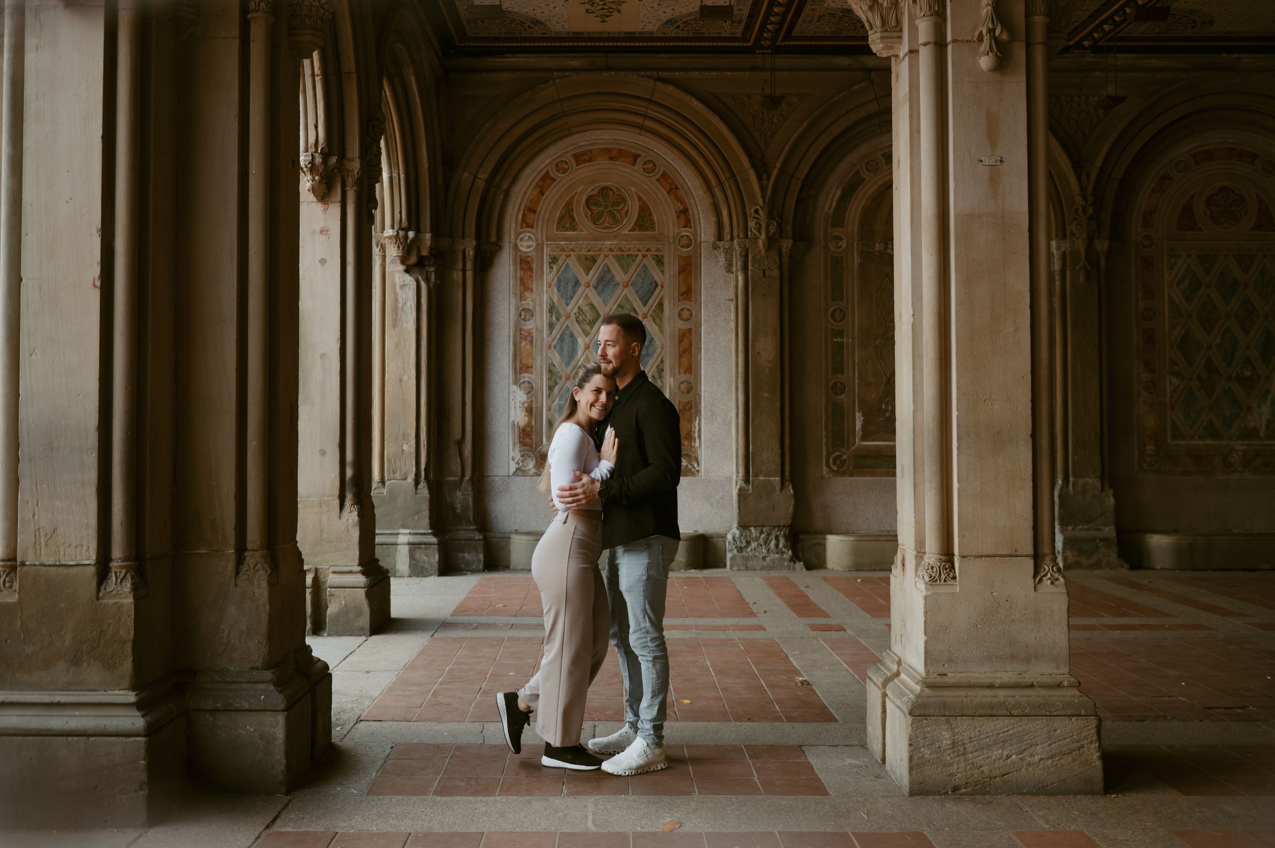 Two people share a romantic moment in an elegant archway with classical architectural details.