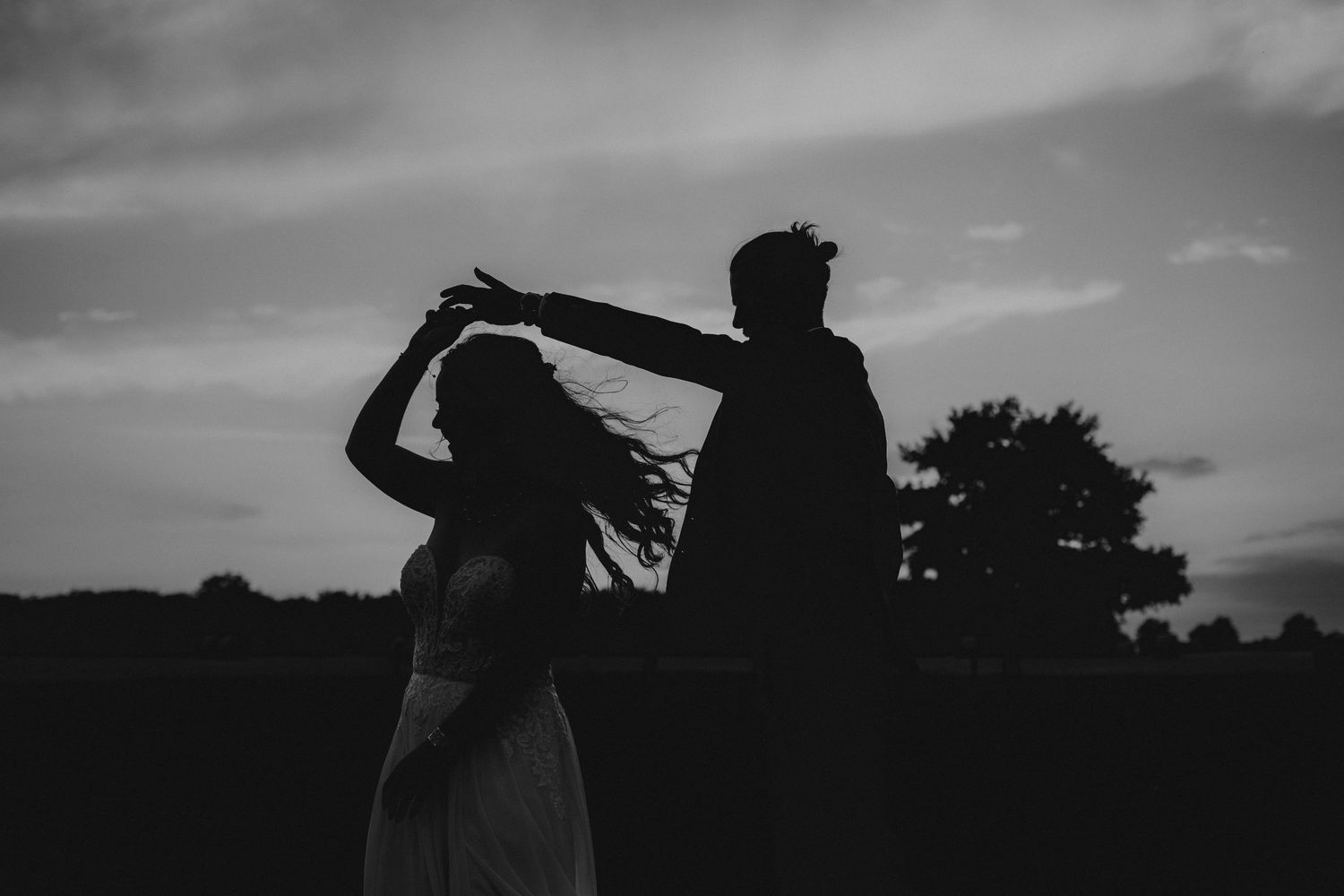 A romantic black and white wedding photograph showing a tender embrace in a natural outdoor setting.