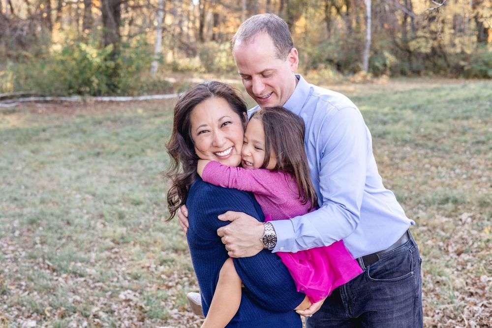 Family of three sharing joyful embrace outdoors in autumn setting.
