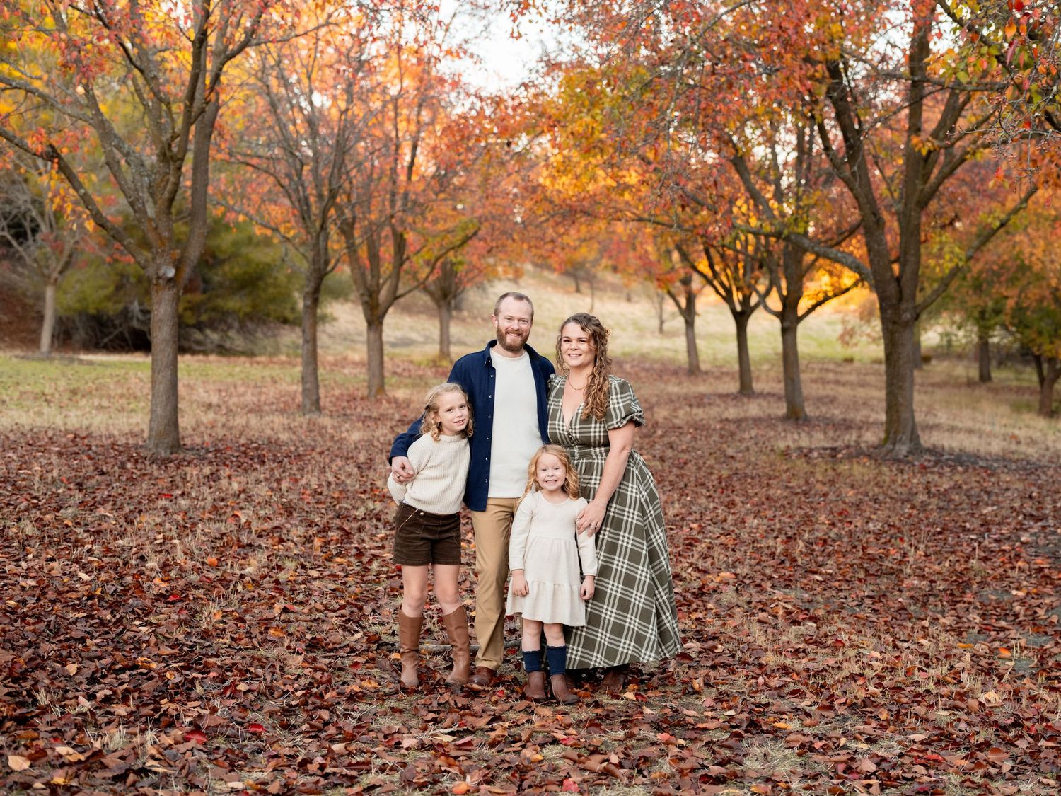Fall season family photoshoot with colorful autumn leaves covering the ground in a scenic park setting.