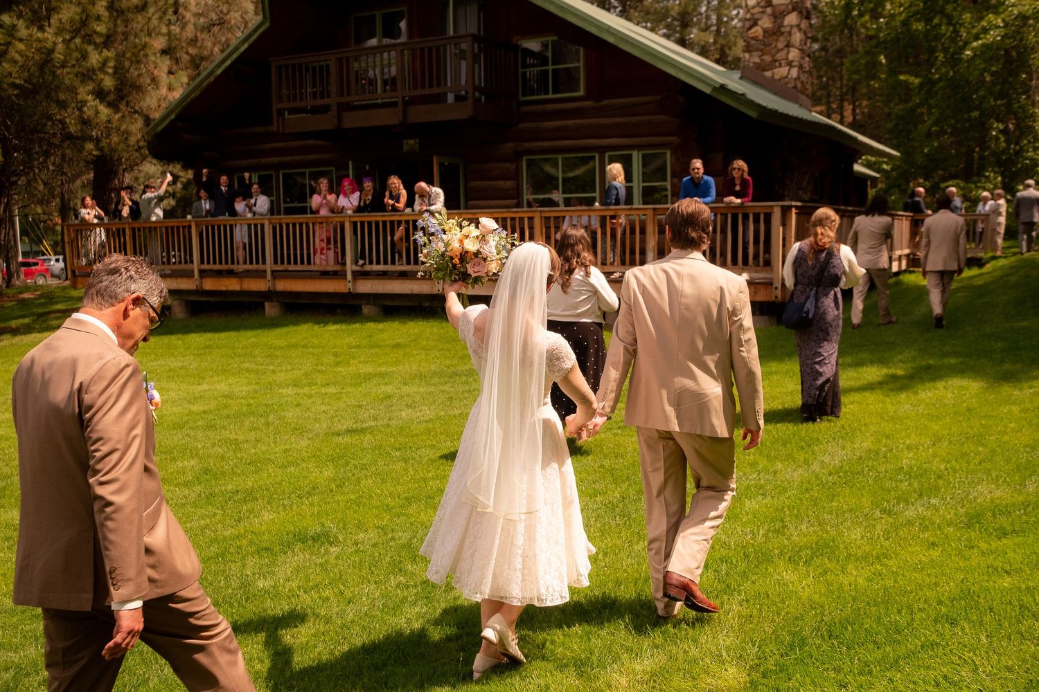 Outdoor wedding scene with guests gathered at a rustic log cabin venue.