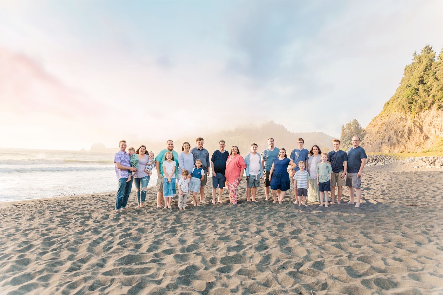 Wedding party and guests lined up for photos on a sandy beach at sunset.
