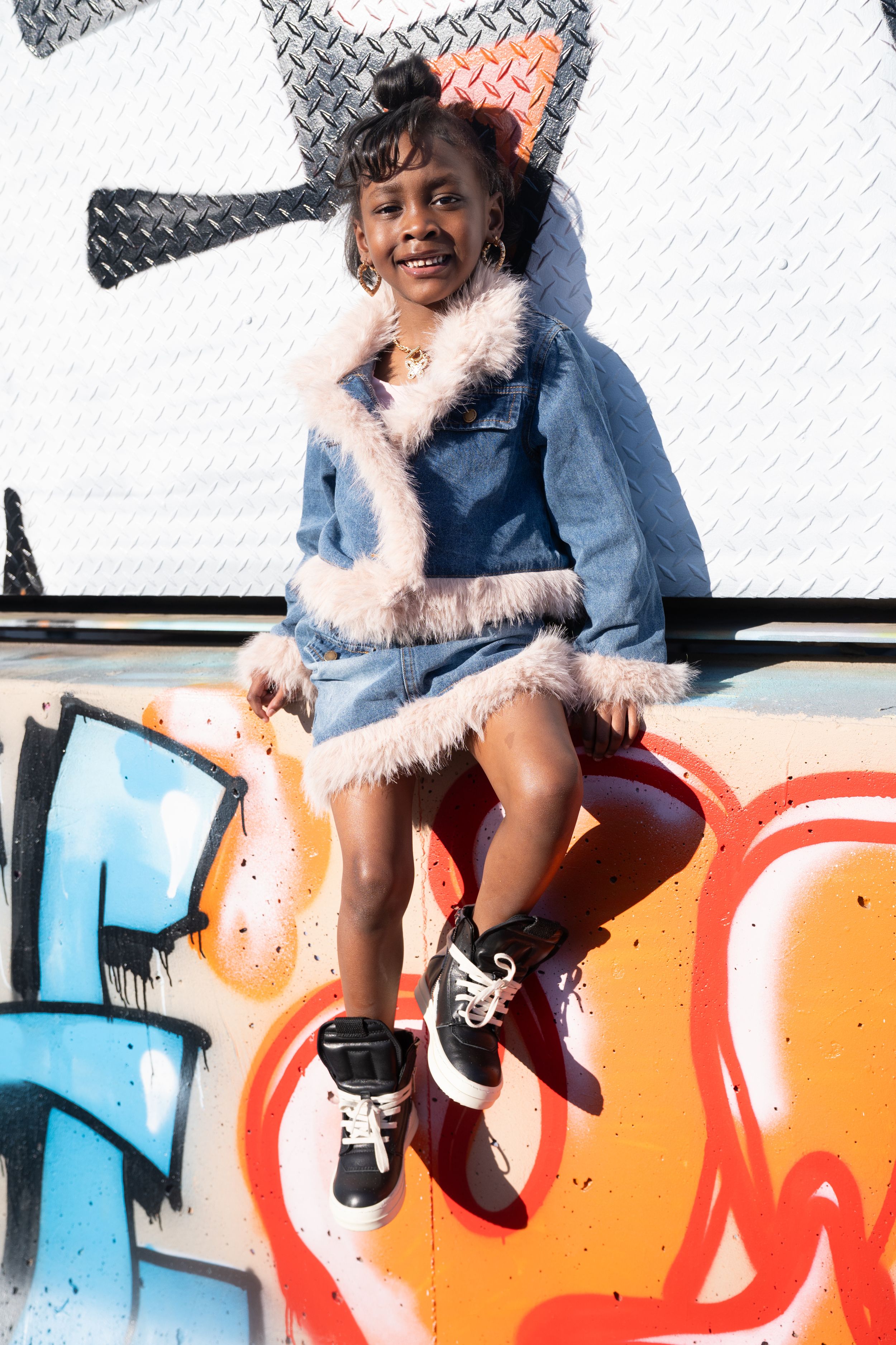 Person sitting on colorful graffiti wall wearing blue denim jacket and black shoes, captured in multiple poses.