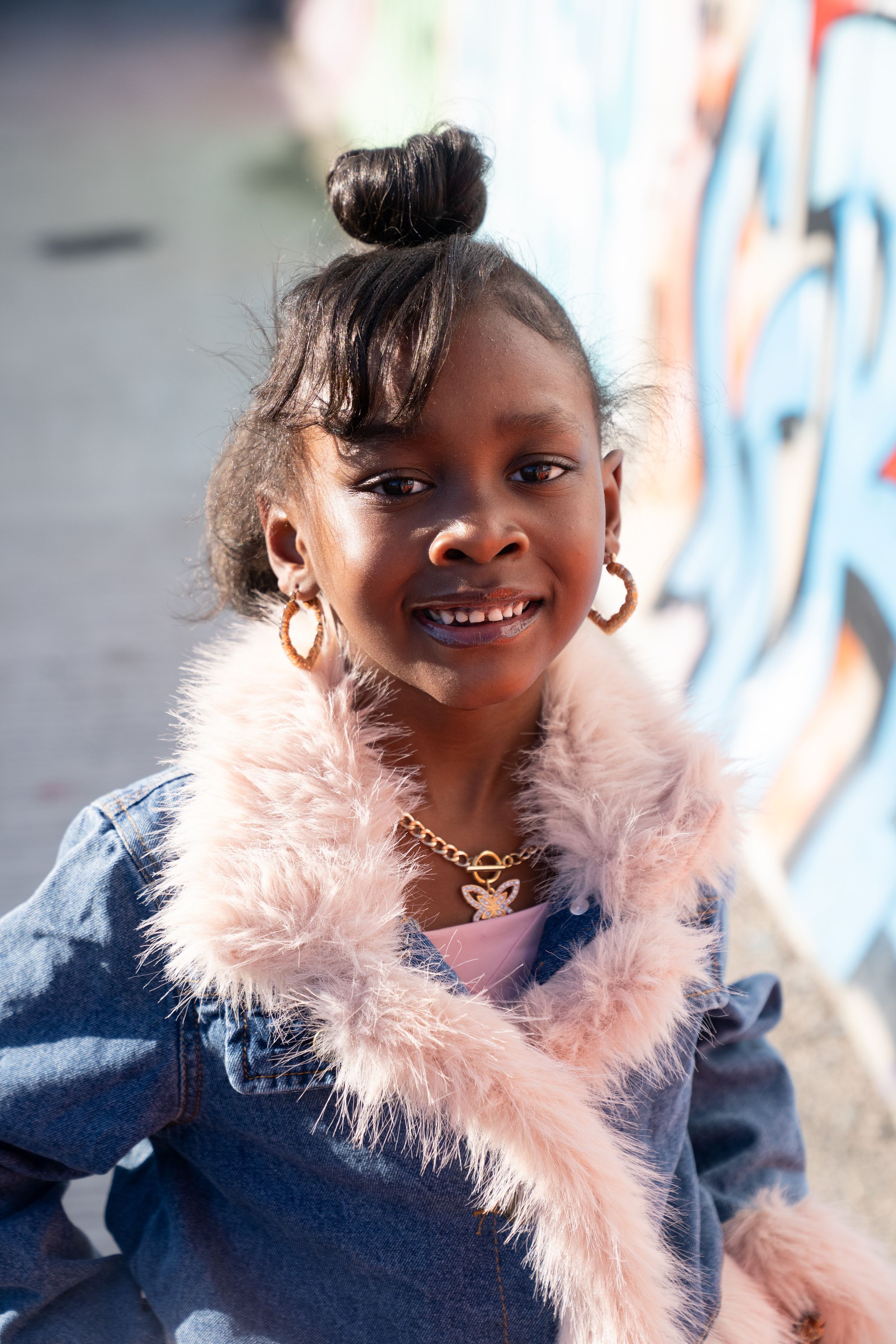 A cheerful child wearing a navy dress with a soft pink feather boa poses for a series of playful portraits.