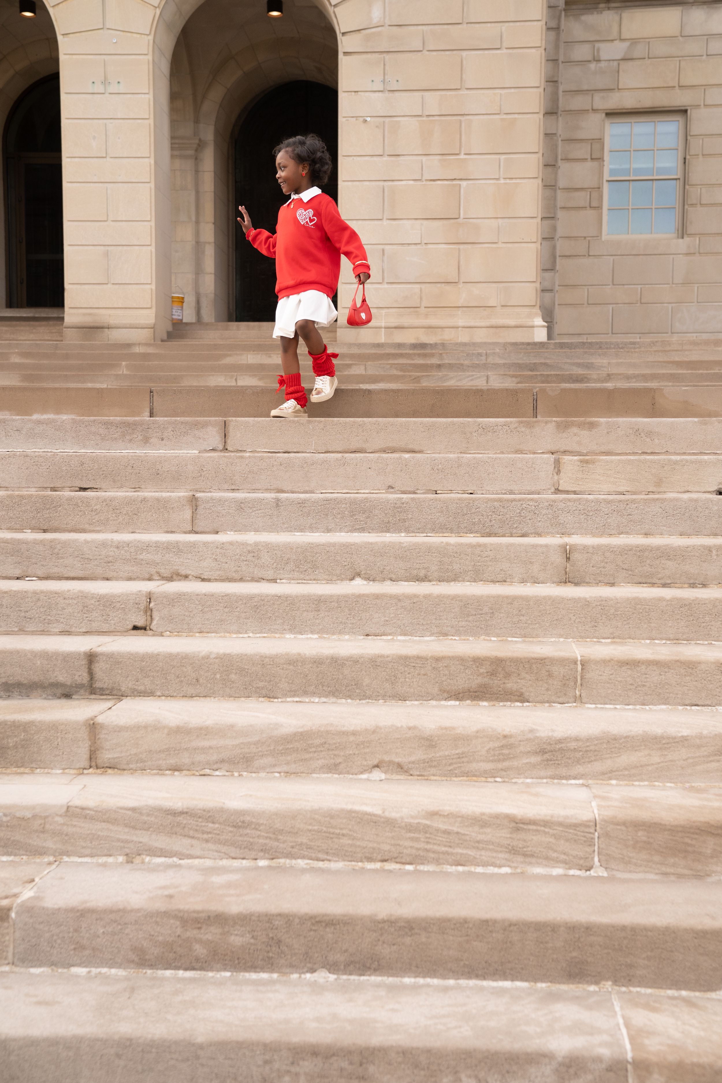 A figure in a red shirt walks along textured concrete steps outside a stone building.