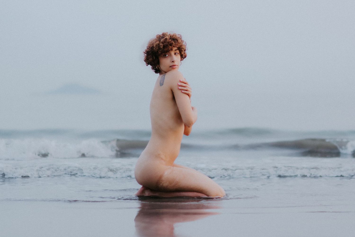 Artistic photo of a figure sitting in shallow ocean waves at dusk.