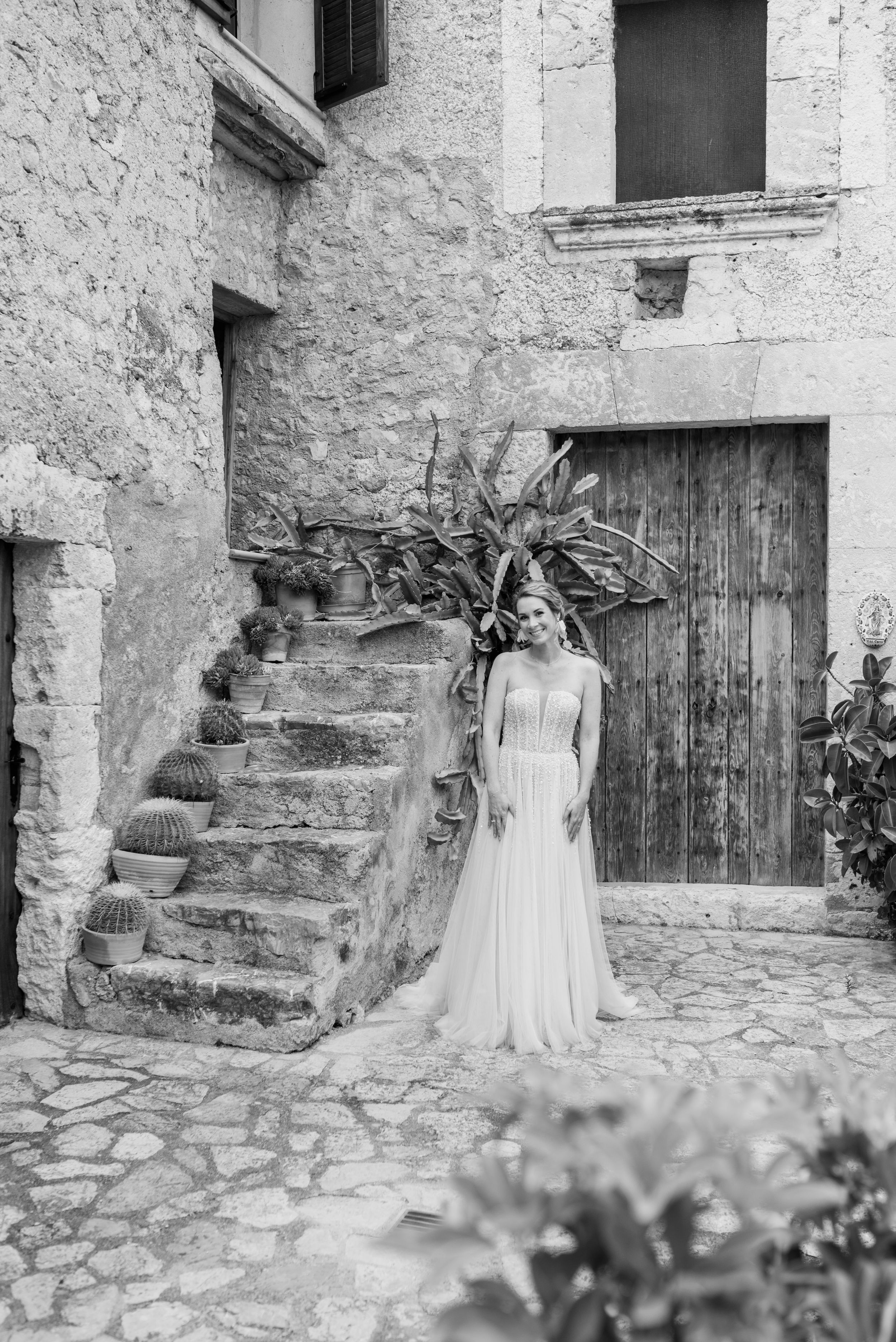 In einem schwarz-weiß-Bild wartet die Braut vor einer mallorquinischen Steintreppe im Innenhof der Finca Xiclati auf den First Look.