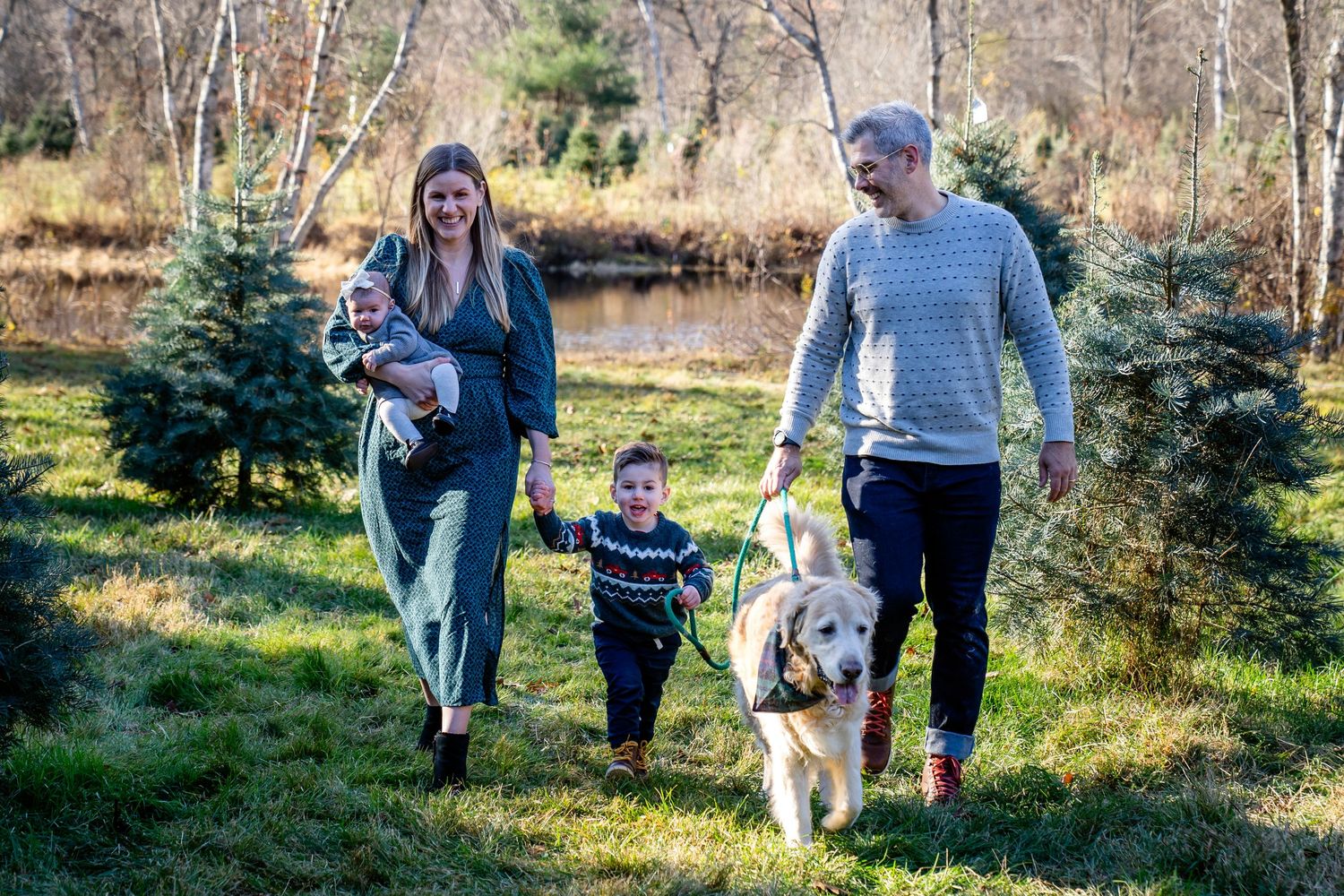 A family takes a winter stroll together with their dog through evergreen trees on a sunny afternoon.