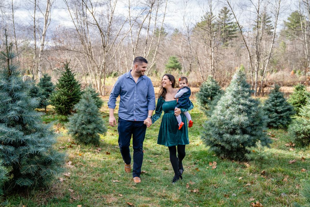 Group of people walking through rows of evergreen trees at a Christmas tree farm on a crisp winter day.