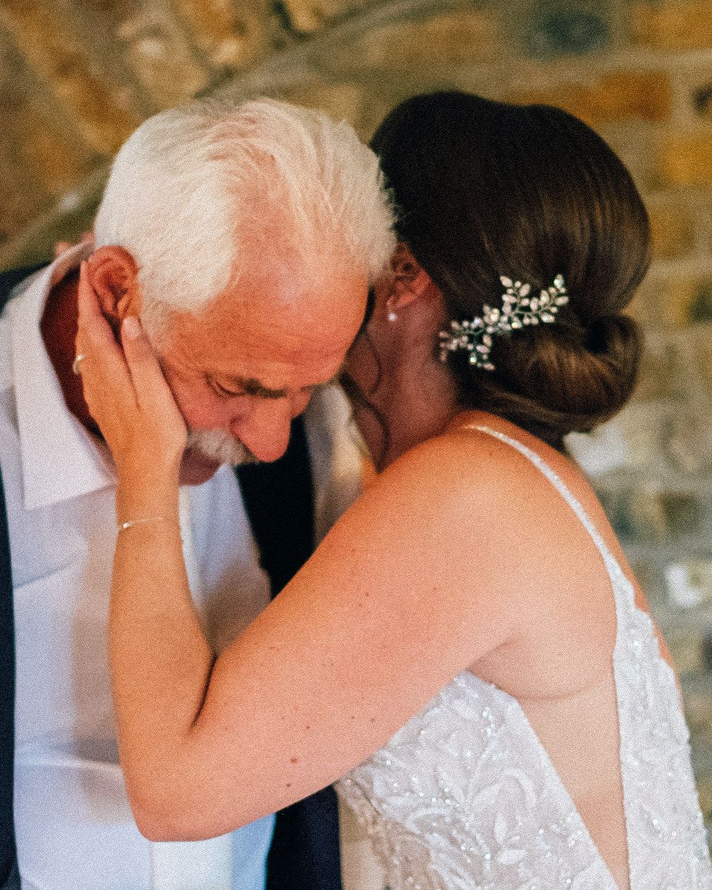 A tender moment at a wedding as a person in a white dress embraces an older loved one wearing light colored attire.