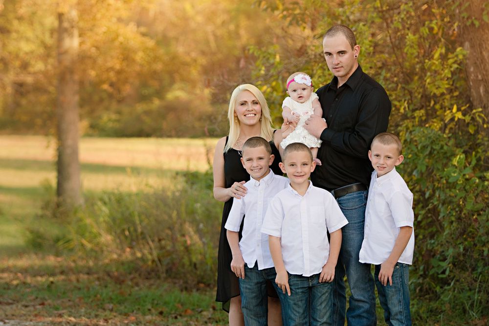 A family of six poses together outdoors in white shirts and jeans during golden hour autumn lighting.