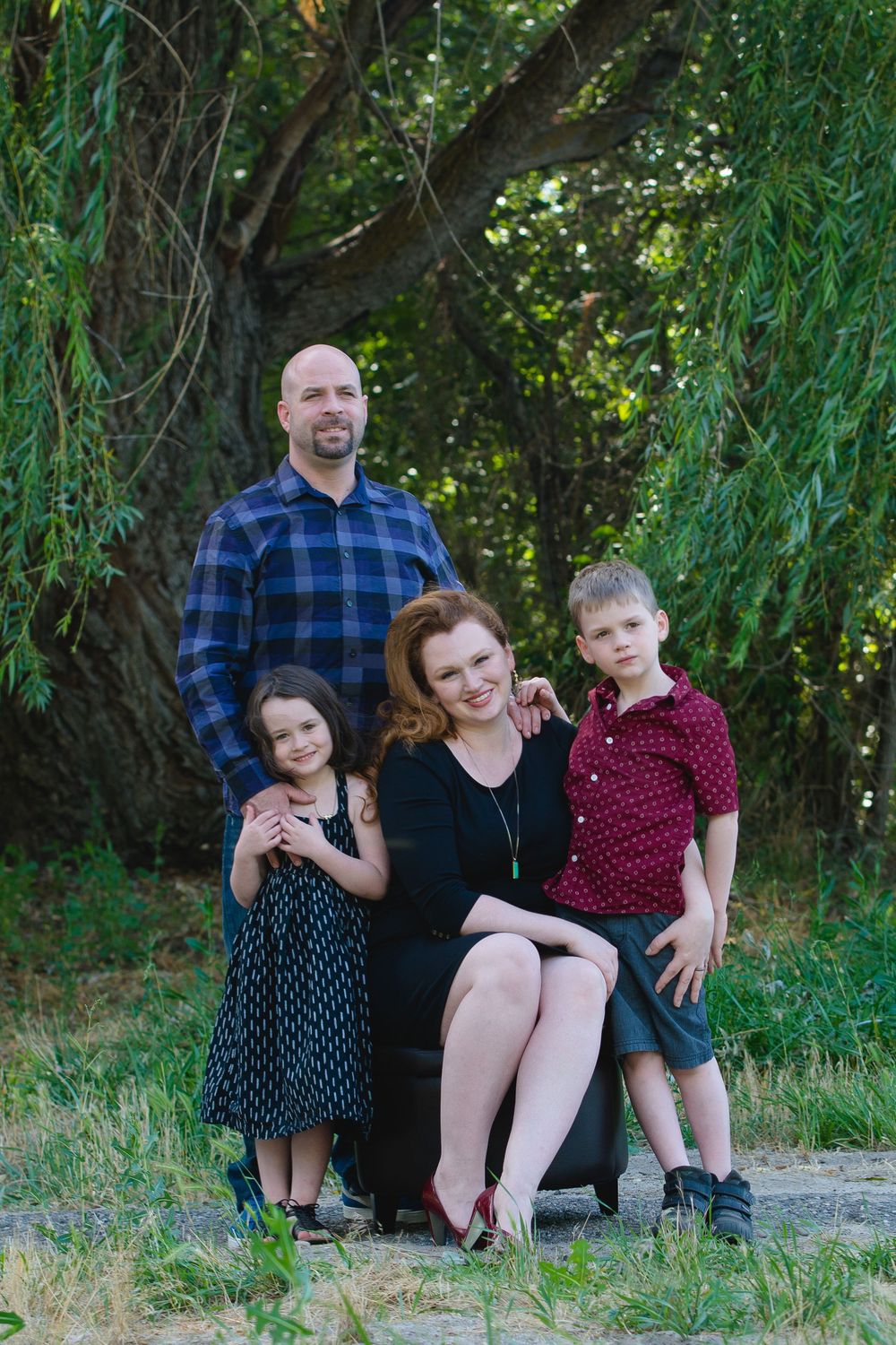 A family of four poses outdoors under a weeping willow tree on a summer evening.