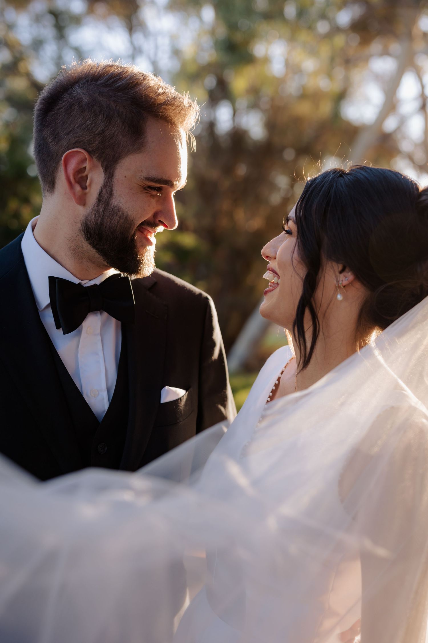 A joyful wedding moment between newlyweds sharing a loving glance outdoors on their special day.