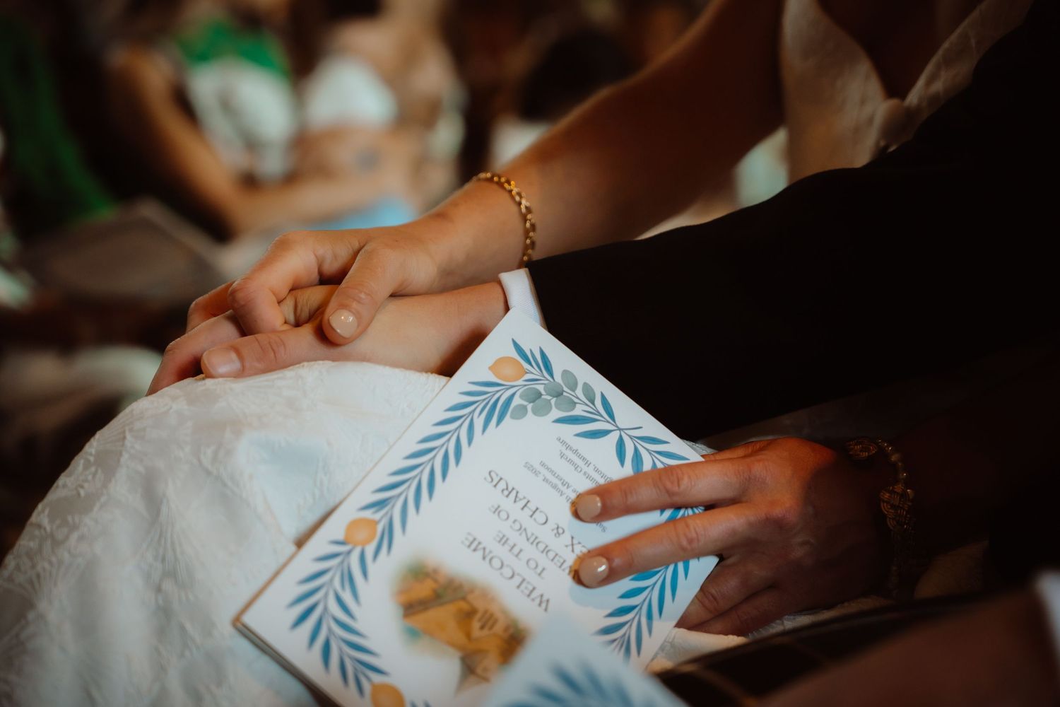Hands hold an elegantly designed white invitation card with delicate blue leaf border pattern at an event.