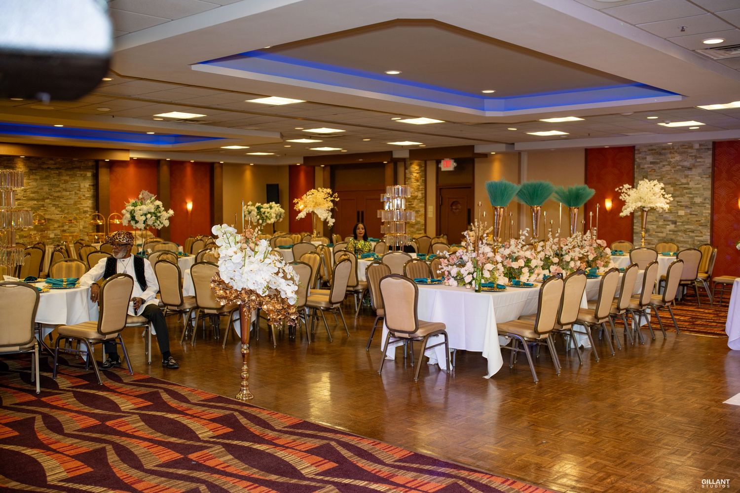 Elegant banquet hall setup with round tables, white linens, stone walls and floral centerpieces for a formal event.